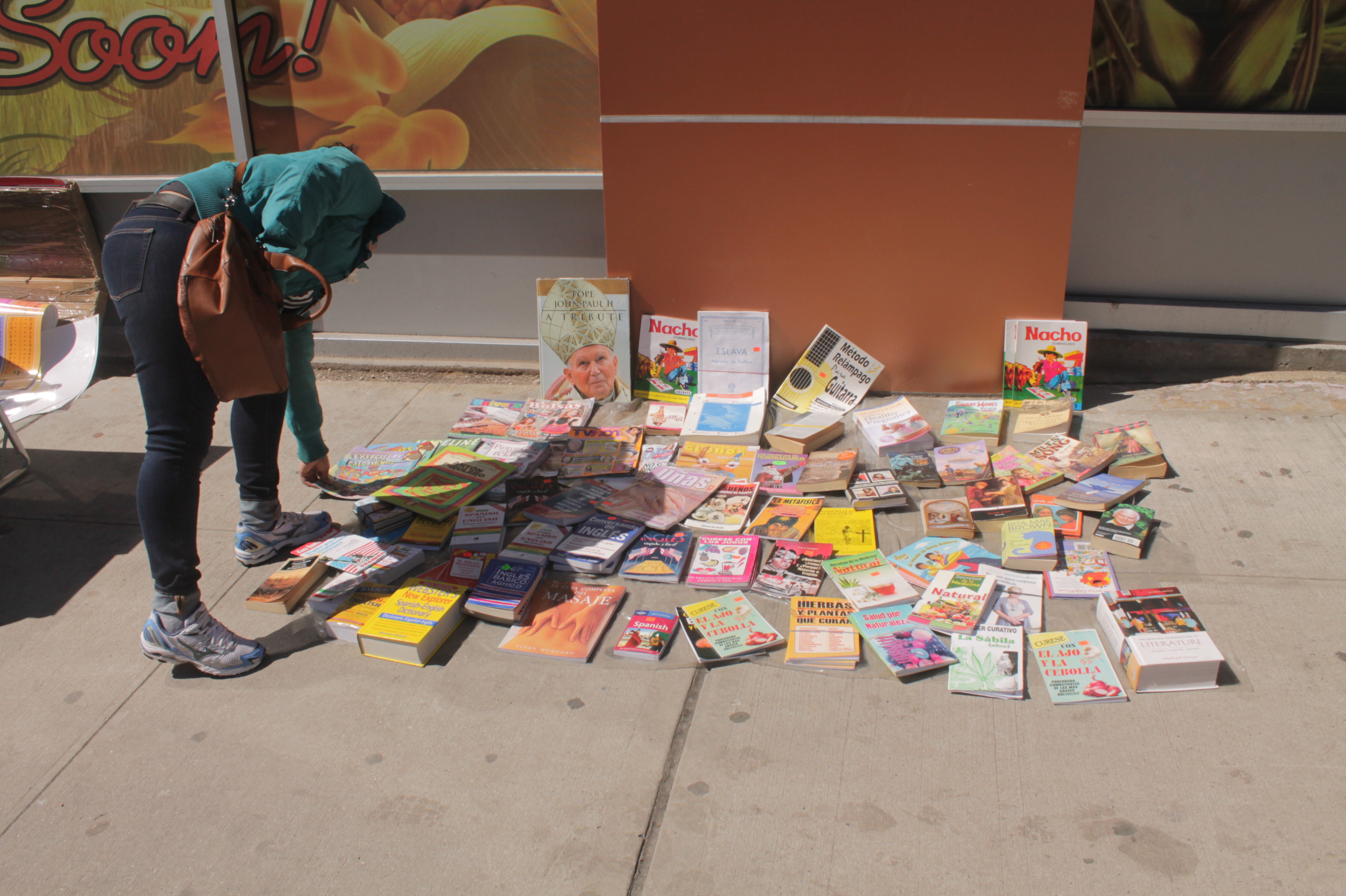 Photograph of a woman browsing through a pile of books for sale on the sidewalk